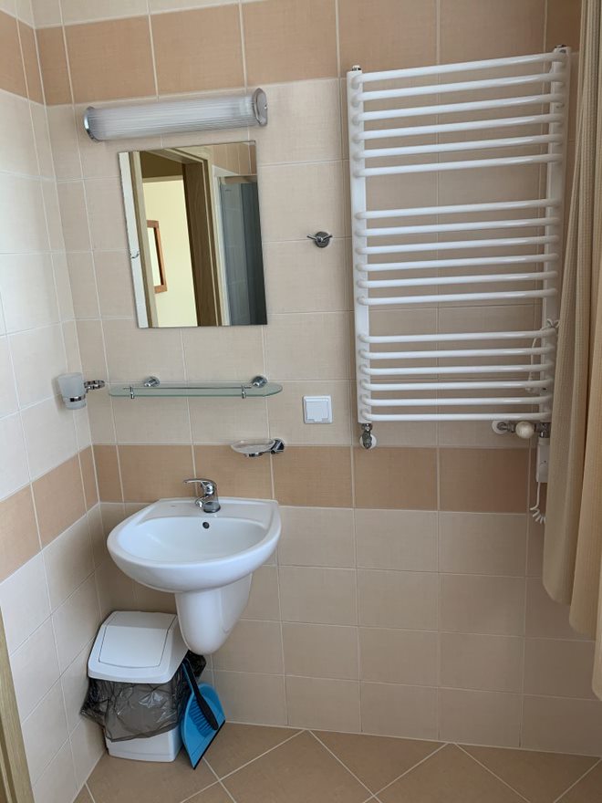 Zdjęcie przedstawia wnętrze łazienki z umywalką i lustrem. Obok na ścianie wisi grzejnik.