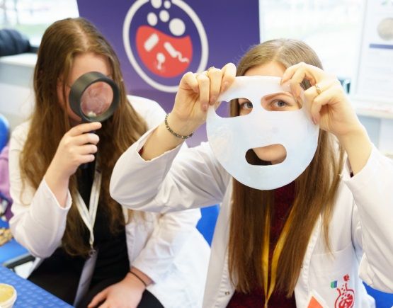 Dwie studentki - jedna z lupą a druga z przedmiotem w kształcie maski.